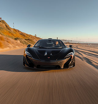 A sleek 2015 Mclaren P1 sold at Sandbox Motors driving along a scenic coastal highway in Southern California